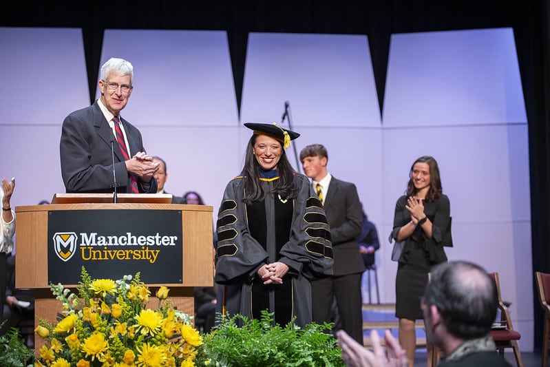Stacy Young stands in academic regalia as audience applauds