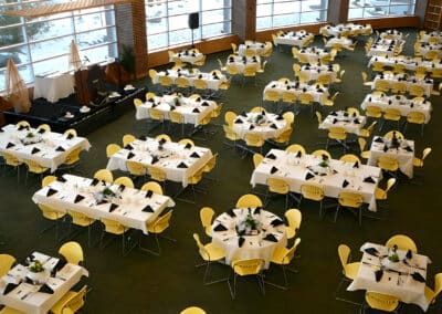 Tables with yellow chairs and black napkins for an indoor event