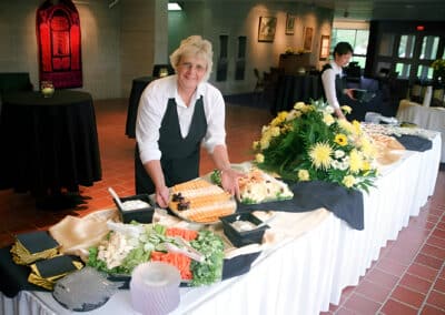 Catering employee smiles next to table of food platters