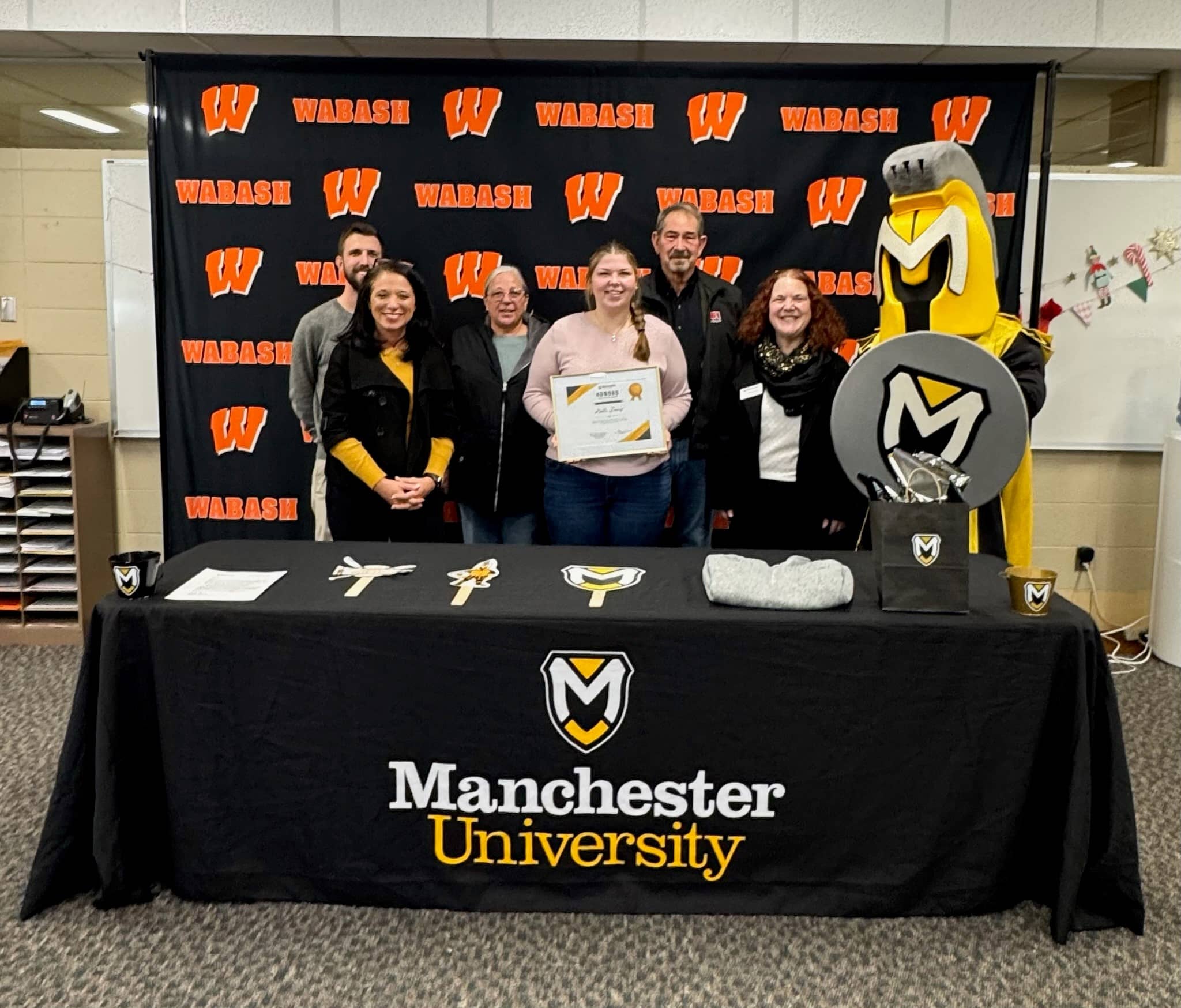 Kalli Davis, parents, MU staff, and mascot Manny stand at table celebrating the Honors Scholarship recipient.