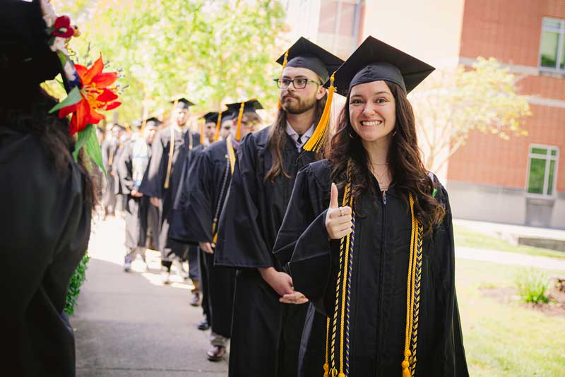 A female student gives the thumbs up sign while walking toward graduation at Manchester University