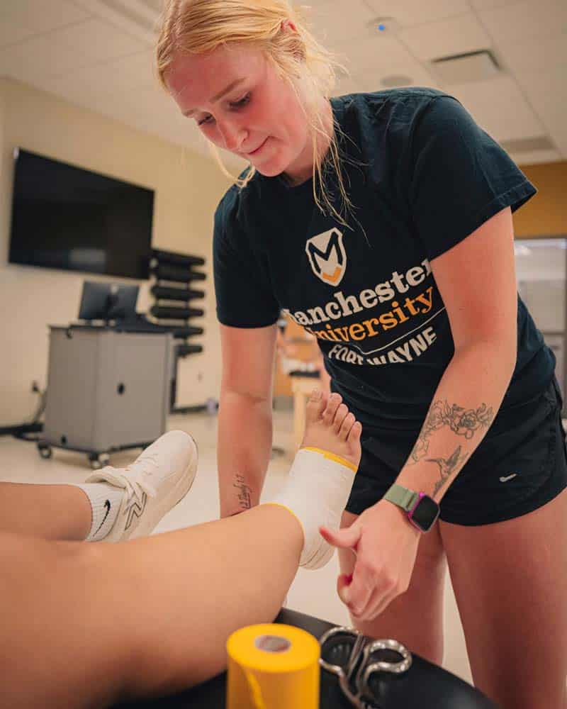 Femal MAT student wraps an ankle with yellow/gold tape.